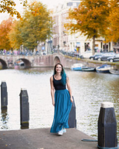 traveling photographer wanderstruck ella poses in a blue skirt on a dock along one of Amsterdam's canals