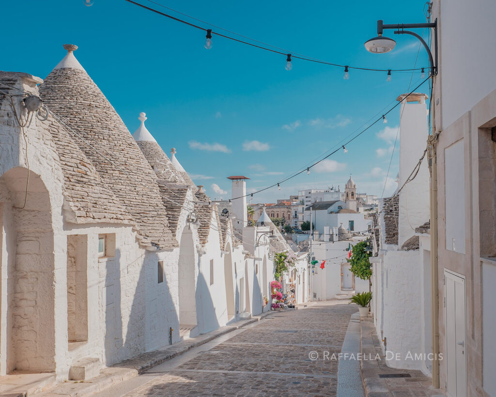 improve your travel photography and confidently take photos like this one of a trulli lined street in Alberobello