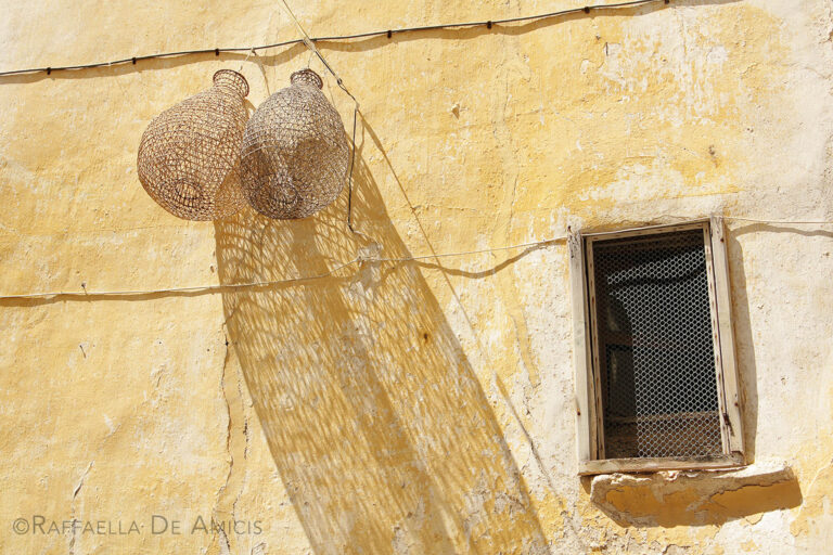 fishing baskets hang on a yellow stucco wall in the old town of Gallipoli Italy under a bright midday sun