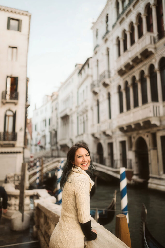 Wanderstruck Ella, a traveling Italian-American photographer smiles next to a canal in Venice Italy