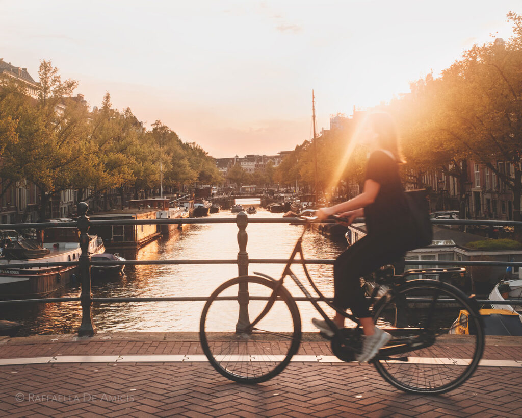 The sun setting over the canal as a girl bikes across the bridge in Amsterdam