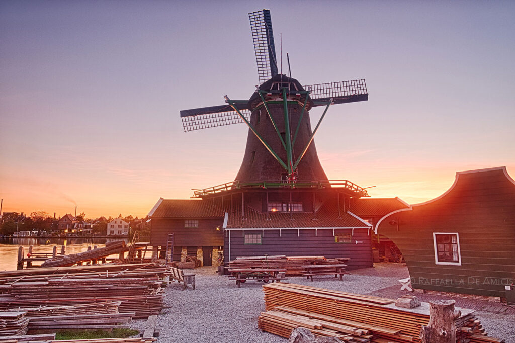 sunset glows behind a windmill at Zaanse Schans outside Amsterdam